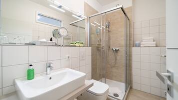 Un baño moderno con lavamanos blanco, inodoro y ducha con mampara de vidrio.