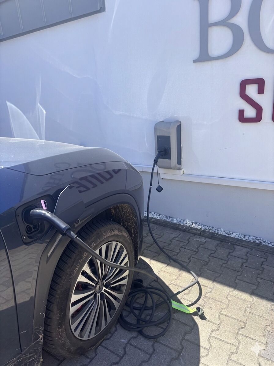A vehicle charging at a station with a wall-mounted box and a cable.
