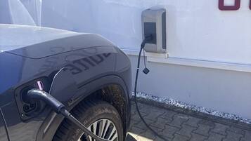 A vehicle charging at a station with a wall-mounted box and a cable.
