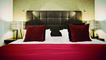Quarto de hotel com uma cama grande, duas almofadas vermelhas, um painel de cabeceira acolchoado e luminárias de cabeceira.