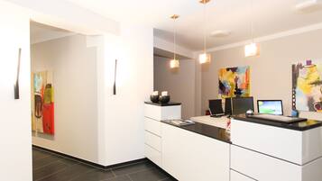 A modern kitchen with white cabinetry, a black countertop, and pendant lighting. There are two computer monitors on the counter.