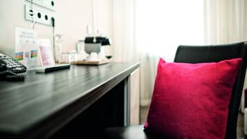 A hotel room with a desk, a telephone, a digital service sign, and a red pillow on a chair.