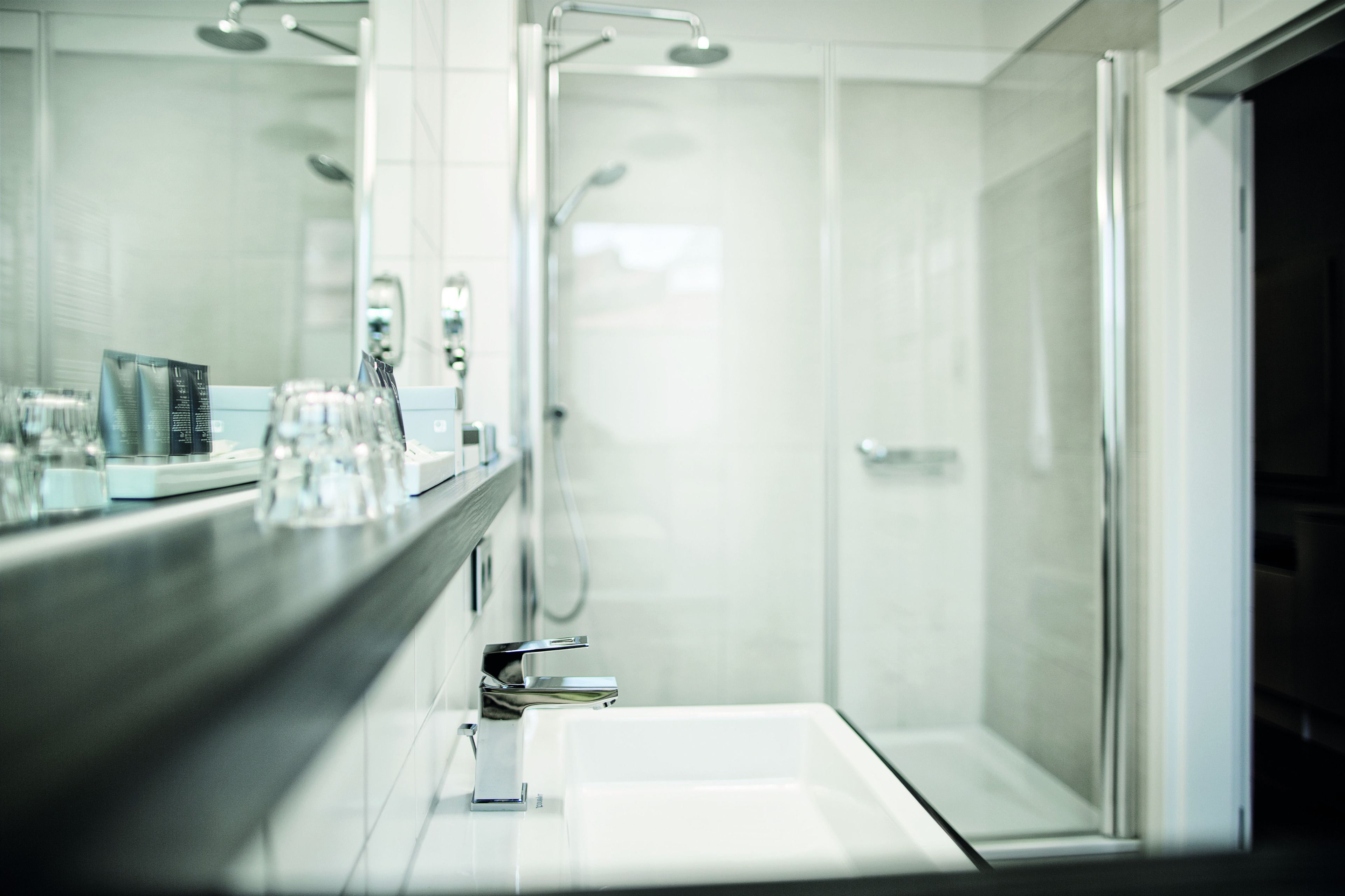 Un baño moderno con cabina de ducha de vidrio, un espejo grande y una encimera con cristalería y artículos de aseo.