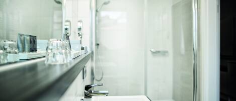 Un baño moderno con cabina de ducha de vidrio, un espejo grande y una encimera con cristalería y artículos de aseo.