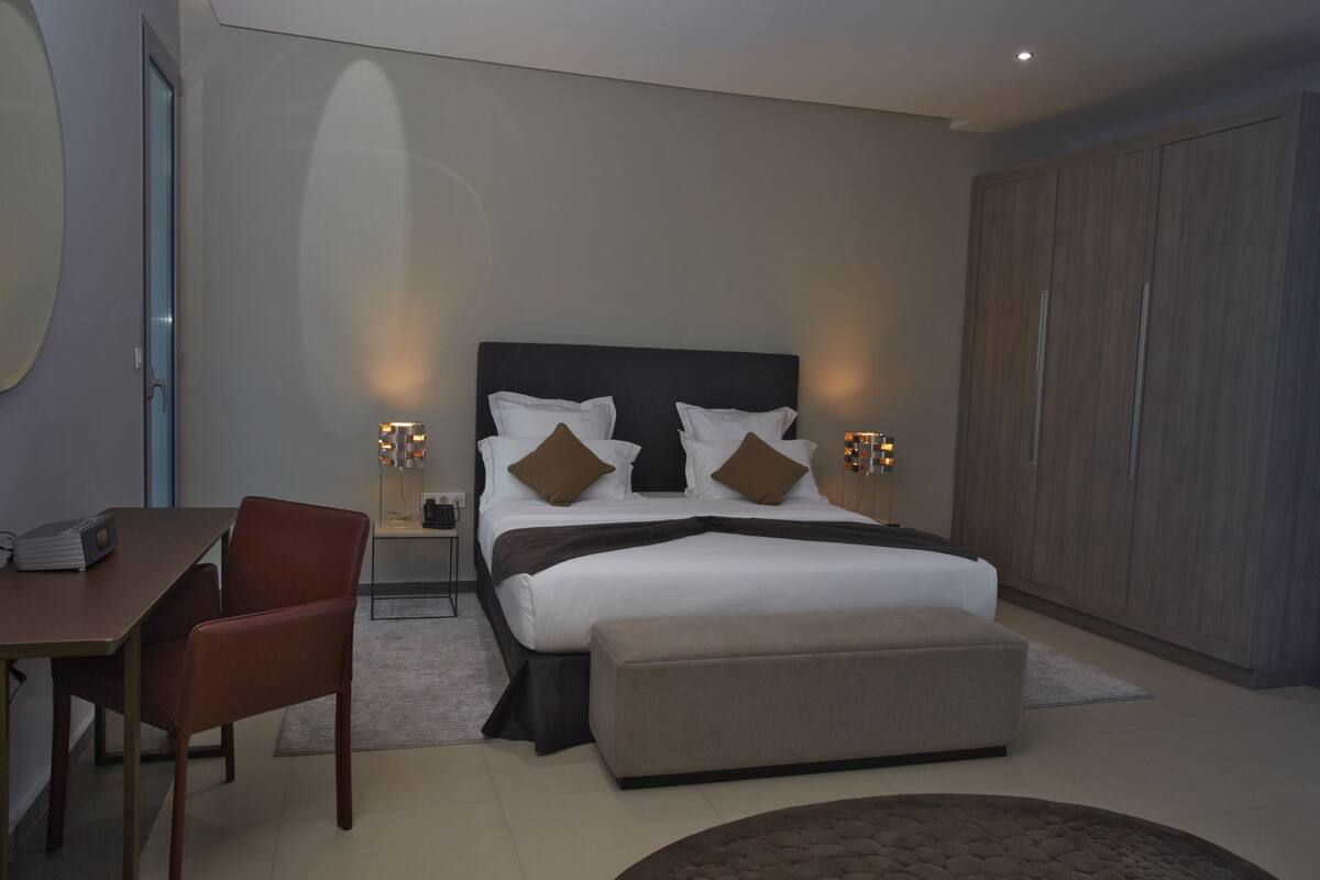 A modern bedroom with a large bed, bedside tables, a desk, and a wardrobe.