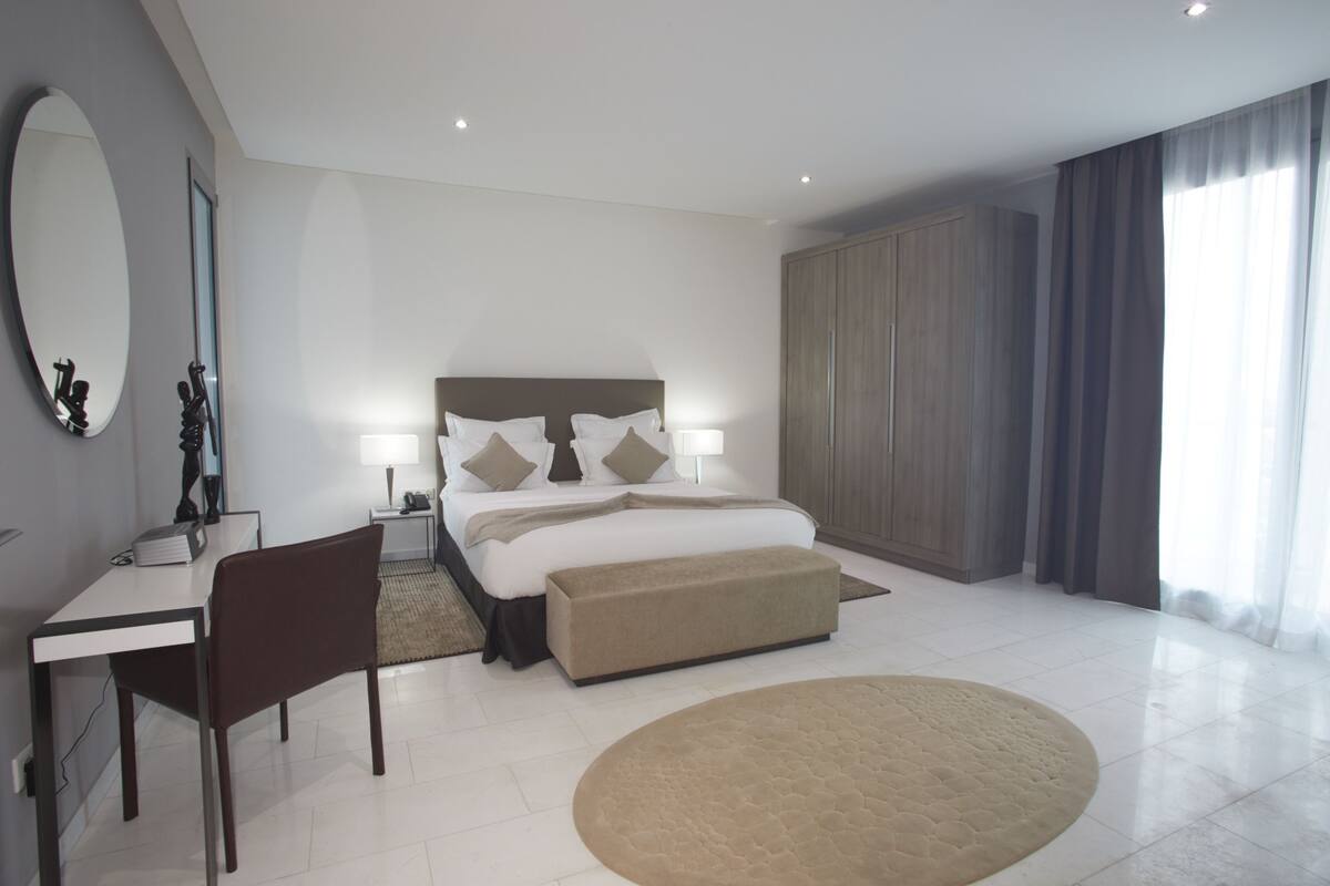 A modern bedroom with a large bed, bedside tables, a desk, and a chair.