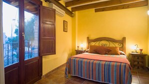 Quarto com cama, cabeceira de madeira, duas mesinhas de cabeceira com abajures, janela com vista e uma porta.