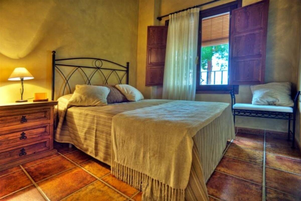 Un dormitori amb un llit, una taula de nit, una panxa i una finestra amb cortines.