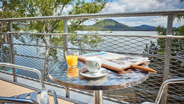 Ein runder Glastisch mit einer Zeitung, einer Tasse und einem Glas Orangensaft.