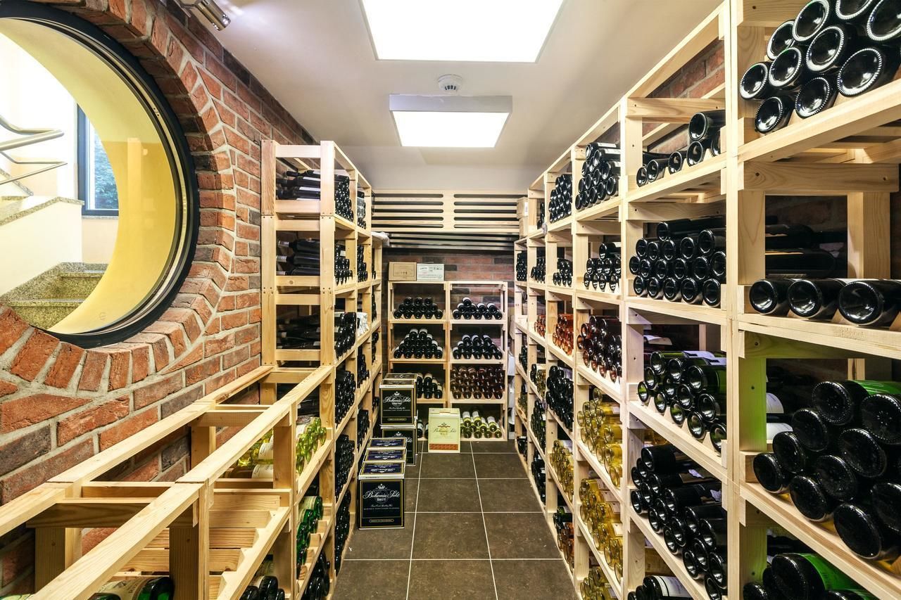 A wine cellar with shelves stocked with wine bottles, a brick wall, and a skylight.