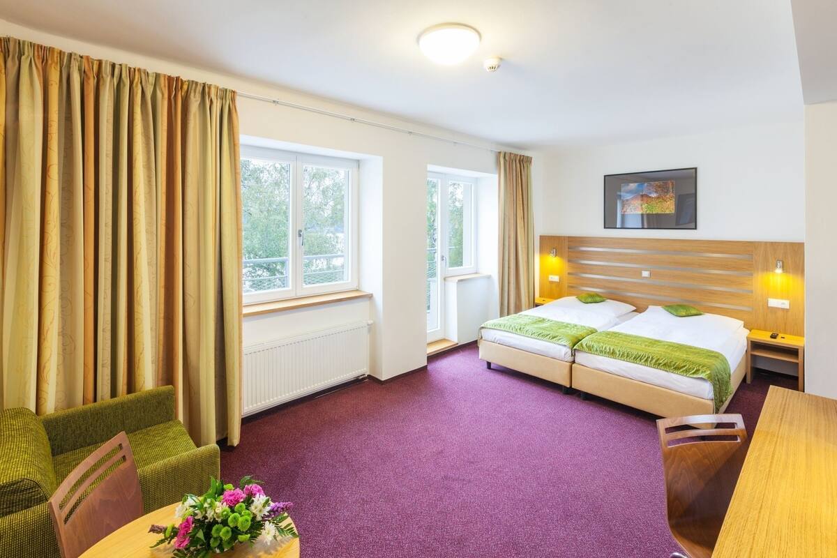A hotel room with a bed, two bedside tables, a chair, a table with flowers, and a window with curtains.