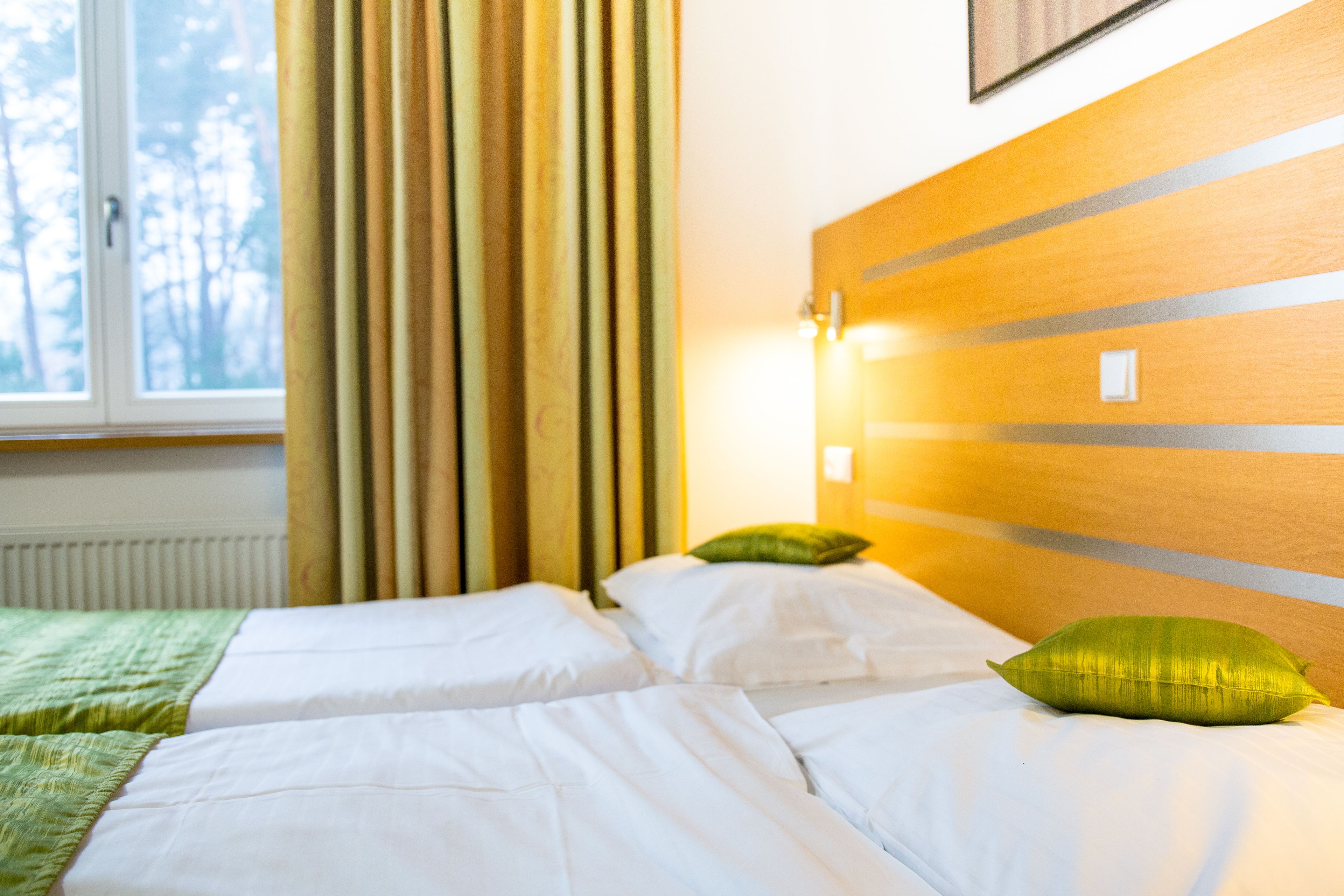 A hotel room with a bed, green pillows, a window with curtains, and a wooden headboard.