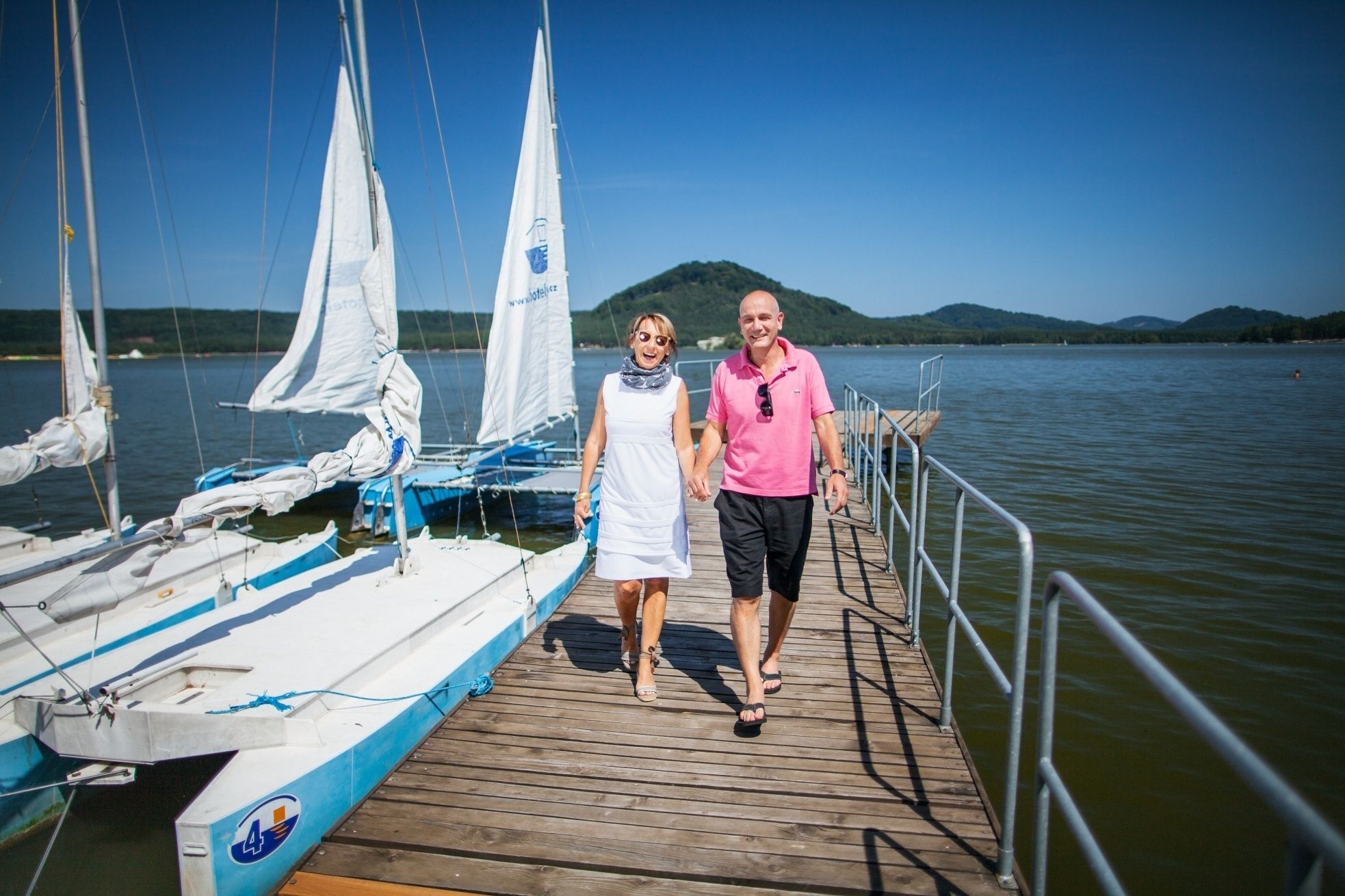 A wooden pier extending into a lake with sailboats docked on the left.