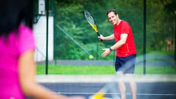 Una cancha de tenis con red, un jugador con camisa roja y una pelota de tenis en movimiento.