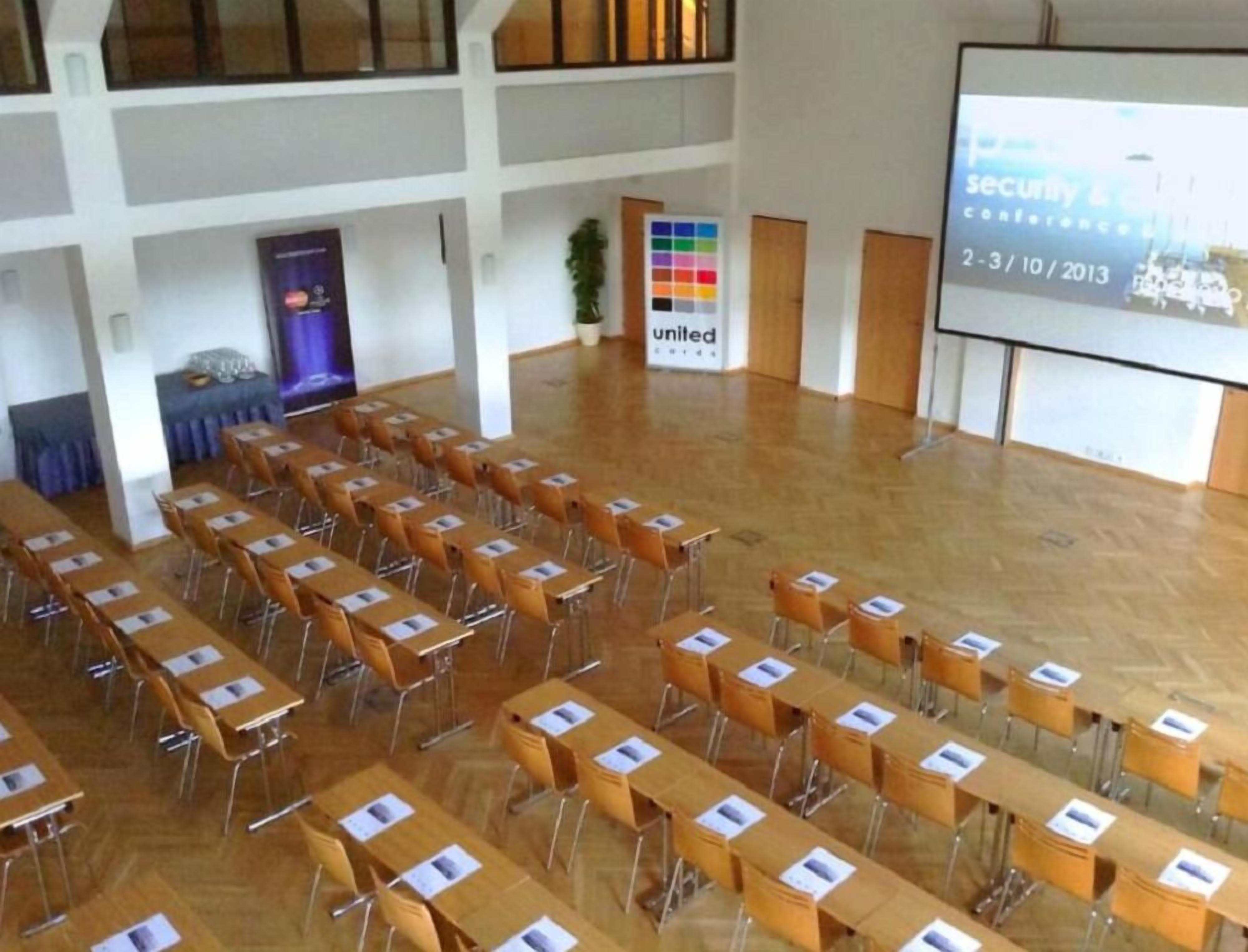 Un salón de conferencias con filas de mesas y sillas, una pantalla de proyector mostrando una presentación y un letrero con la palabra 'United' en la pared.