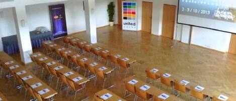 Un salón de conferencias con filas de mesas y sillas, una pantalla de proyector mostrando una presentación y un letrero con la palabra 'United' en la pared.