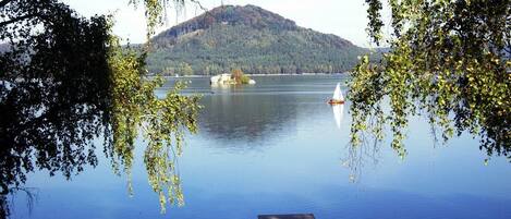 Un lago tranquilo con una pequeña isla y un bote a lo lejos.