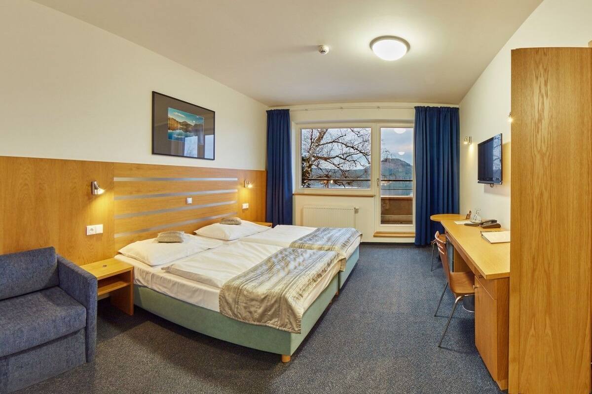 A hotel room with a bed, a desk, a chair, and a TV.