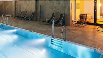 Ein Hallenbad mit klarem Wasser, Liegestühlen und Blick ins Freie.