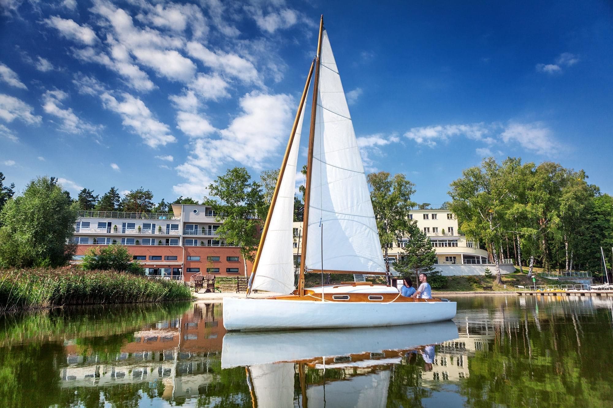 A sailboat on a calm lake with buildings in the background.