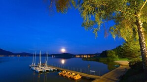 Ein Yachthafen im Abenddämmerung mit vertäuten Booten, eine Mole, die ins ruhige Wasser führt, und ein Baum auf der rechten Seite.