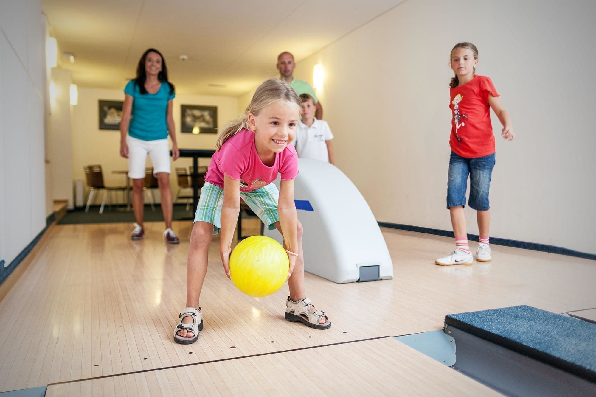 Une salle de bowling avec un plancher en bois, une boule de bowling et plusieurs personnes qui jouent.