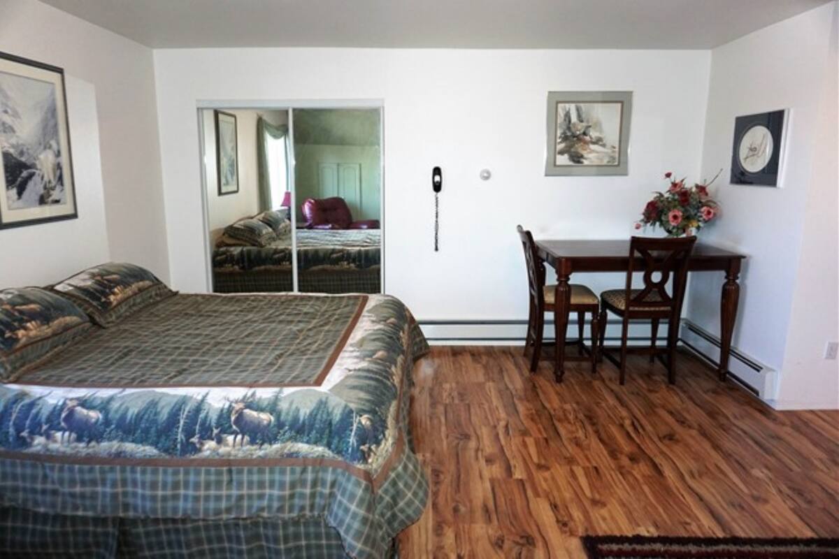 A bedroom with a large bed, a wooden floor, a desk with chairs, and a sliding door leading to another room.