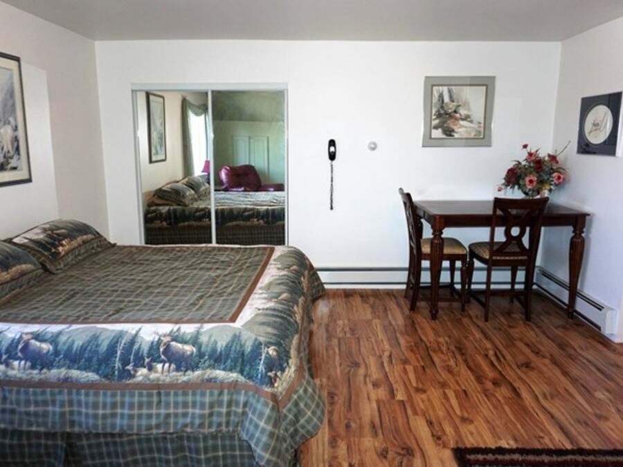 A bedroom with a large bed, a wooden floor, a desk with chairs, and a sliding door leading to another room.