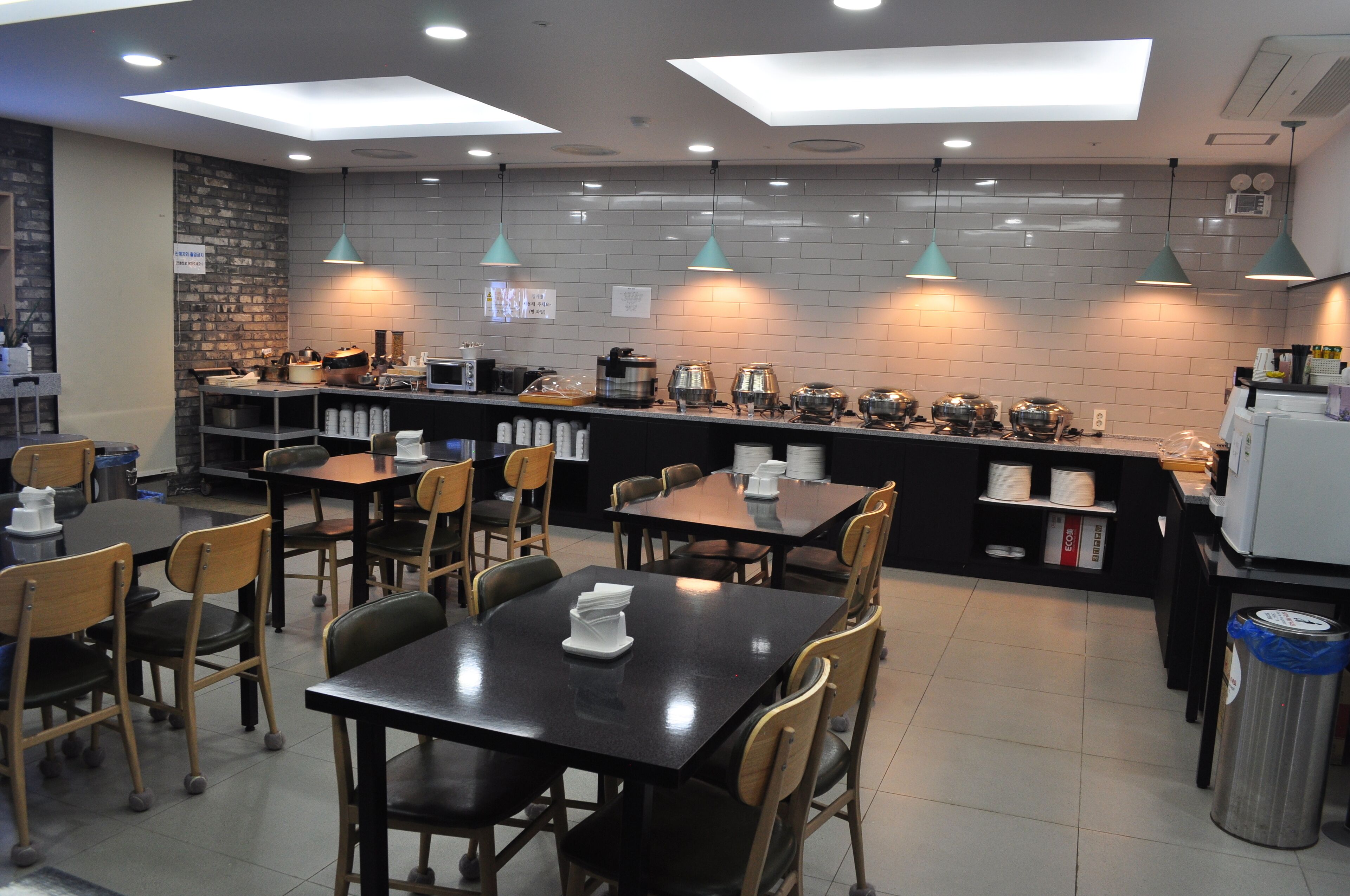 Un café moderne avec des tables noires et des chaises en bois, un comptoir équipé de divers appareils et des luminaires suspendus.