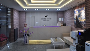 A hotel reception area with a modern design, including a reception desk, seating area, and artwork on the wall. - Hound Hotel Sangmu (Gwangju)