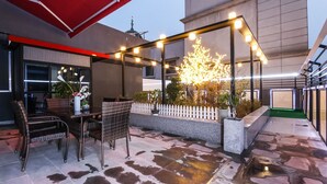 An outdoor patio with wicker furniture, a white picket fence, and a decorative tree under string lights. - Hound Hotel Sangmu (Gwangju)