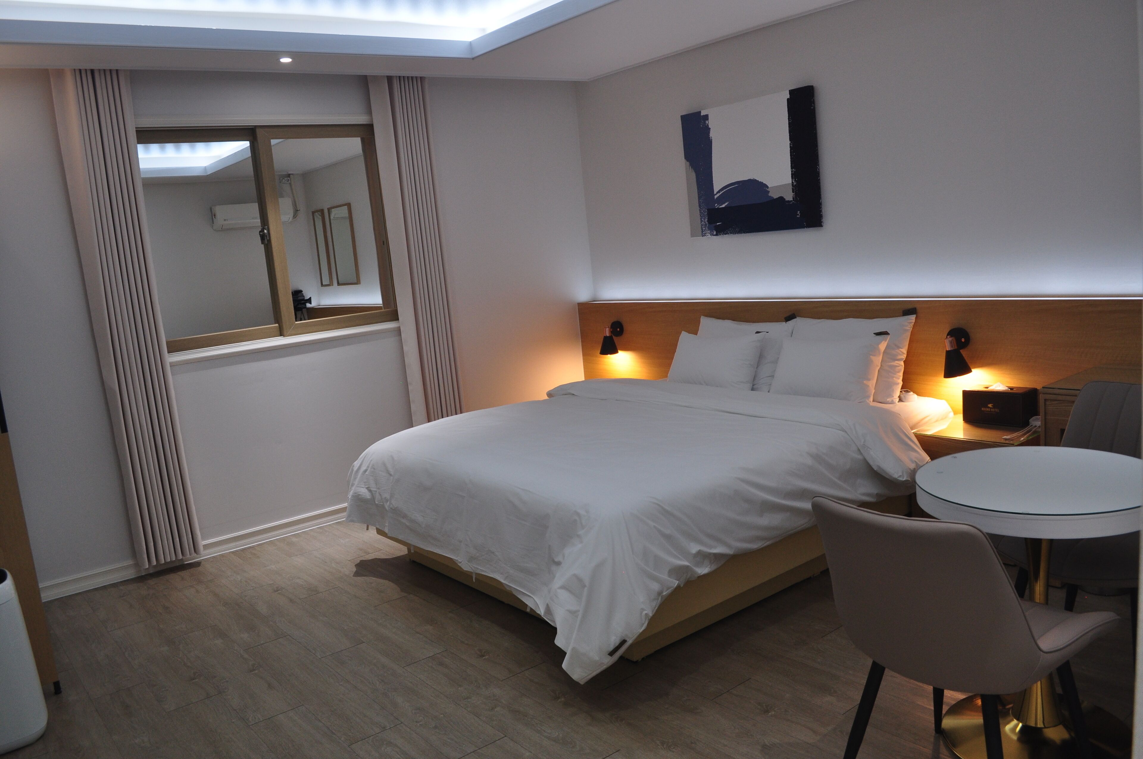 A hotel room with a bed, bedside lamps, a round table, and a chair.