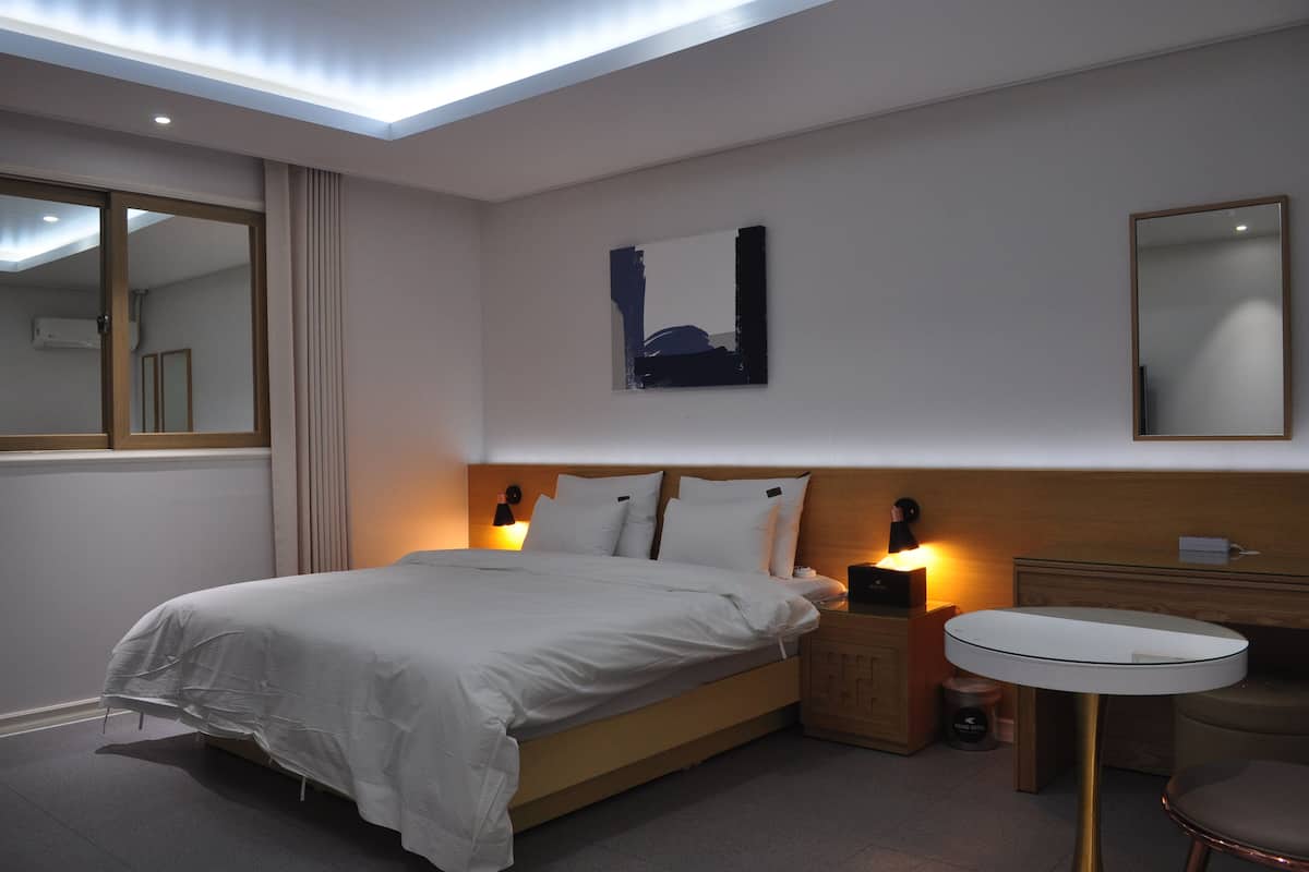 A modern hotel room with a large bed, bedside lamps, a round table, and a mirror.