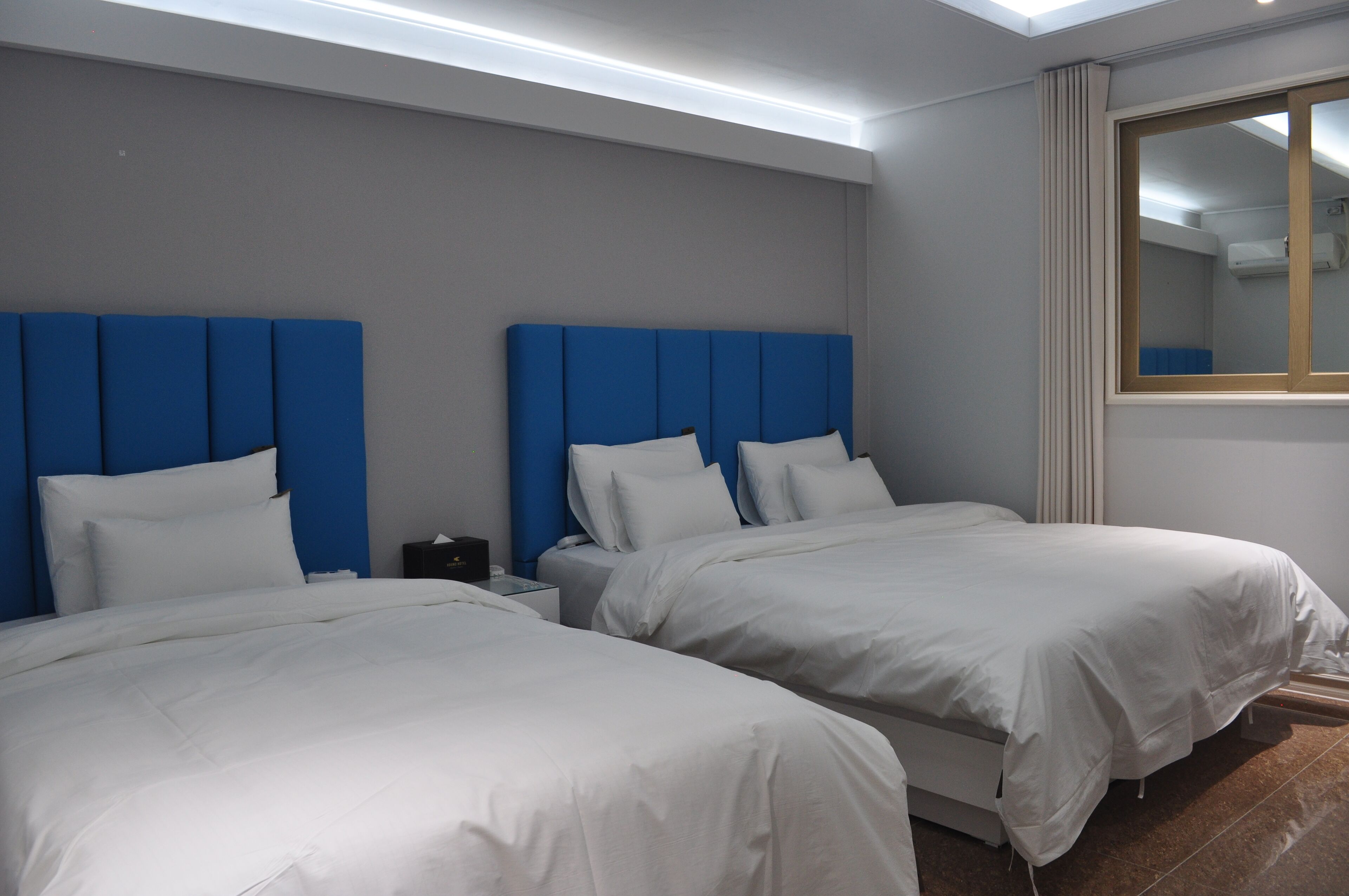 Habitación de hotel con dos camas, cada una con cabecero azul y ropa de cama blanca.