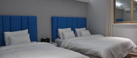 Habitación de hotel con dos camas, cada una con cabecero azul y ropa de cama blanca.
