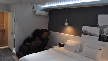 A hotel room with a bed, a massage chair, a nightstand, and a wall-mounted air conditioner.