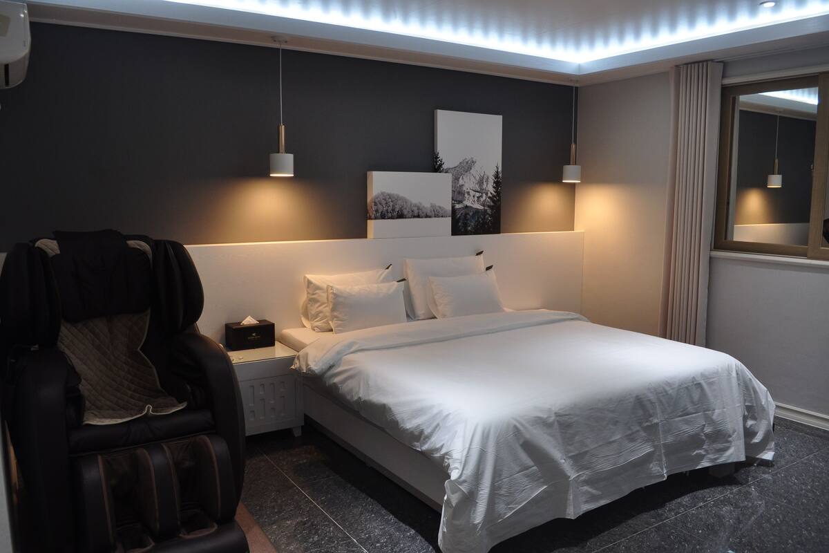 A modern bedroom with a bed, a massage chair, and two pendant lights.