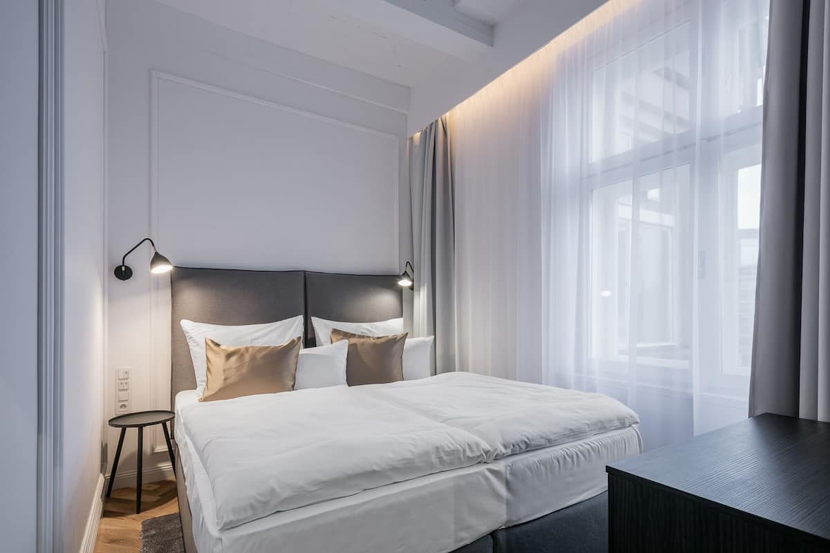 A modern bedroom with a large bed, a bedside table, and a headboard with integrated lighting.