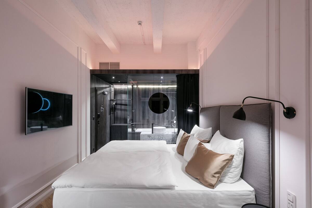 A modern hotel room with a large bed, a TV, a bathroom with a glass door, and a shower area.