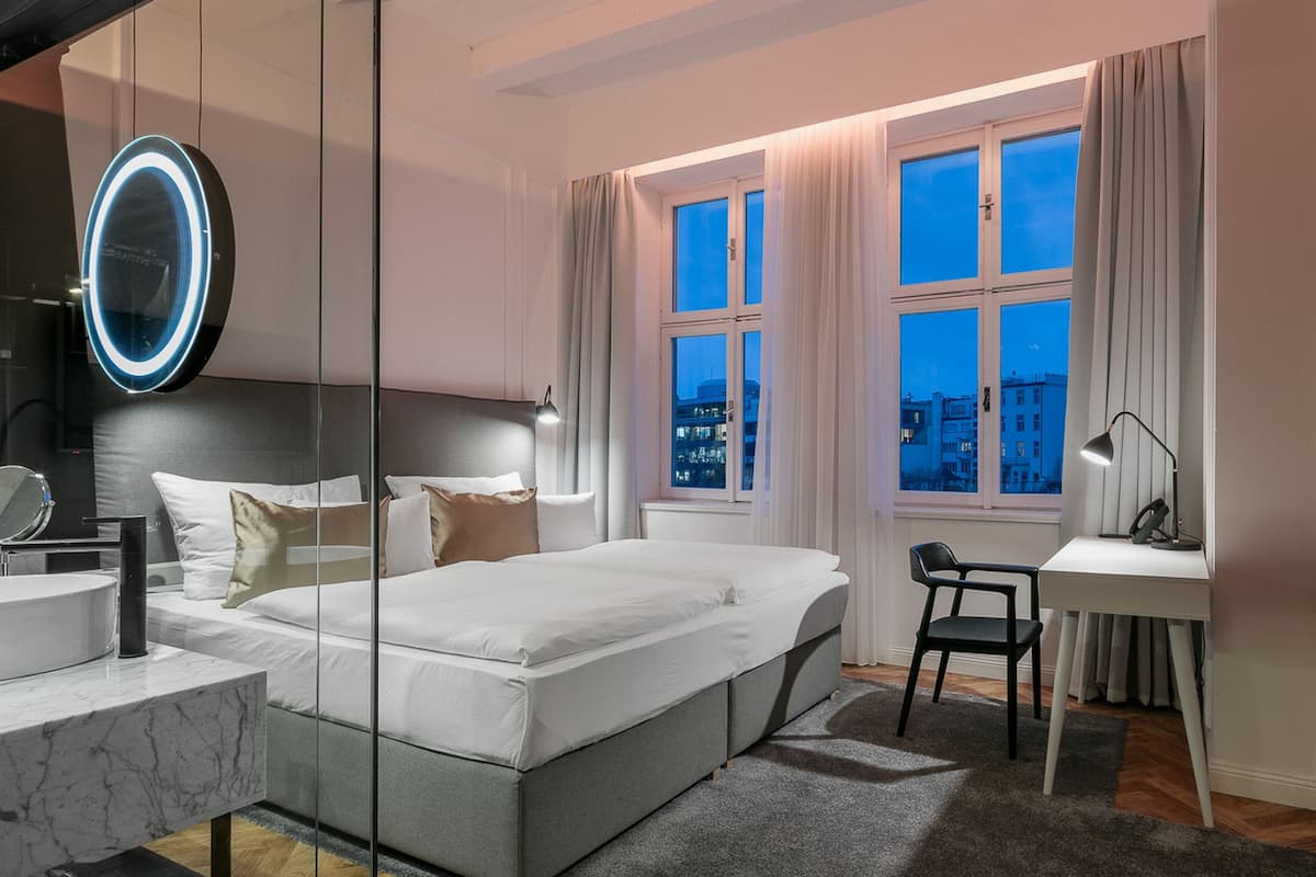 A modern bedroom with a large bed, a desk, and a mirror.