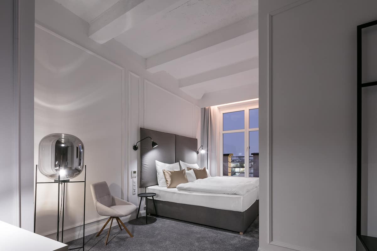 A modern bedroom with a large bed, a standing lamp, a chair, and a floor lamp.