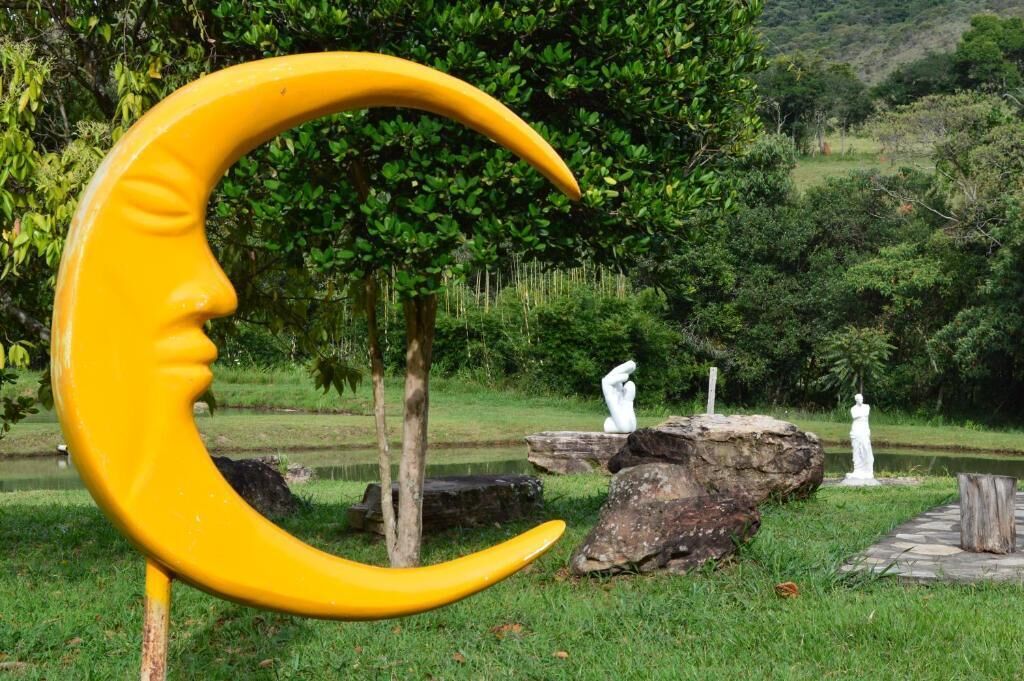 A yellow crescent moon sculpture with a face, surrounded by rocks and trees in a park setting.