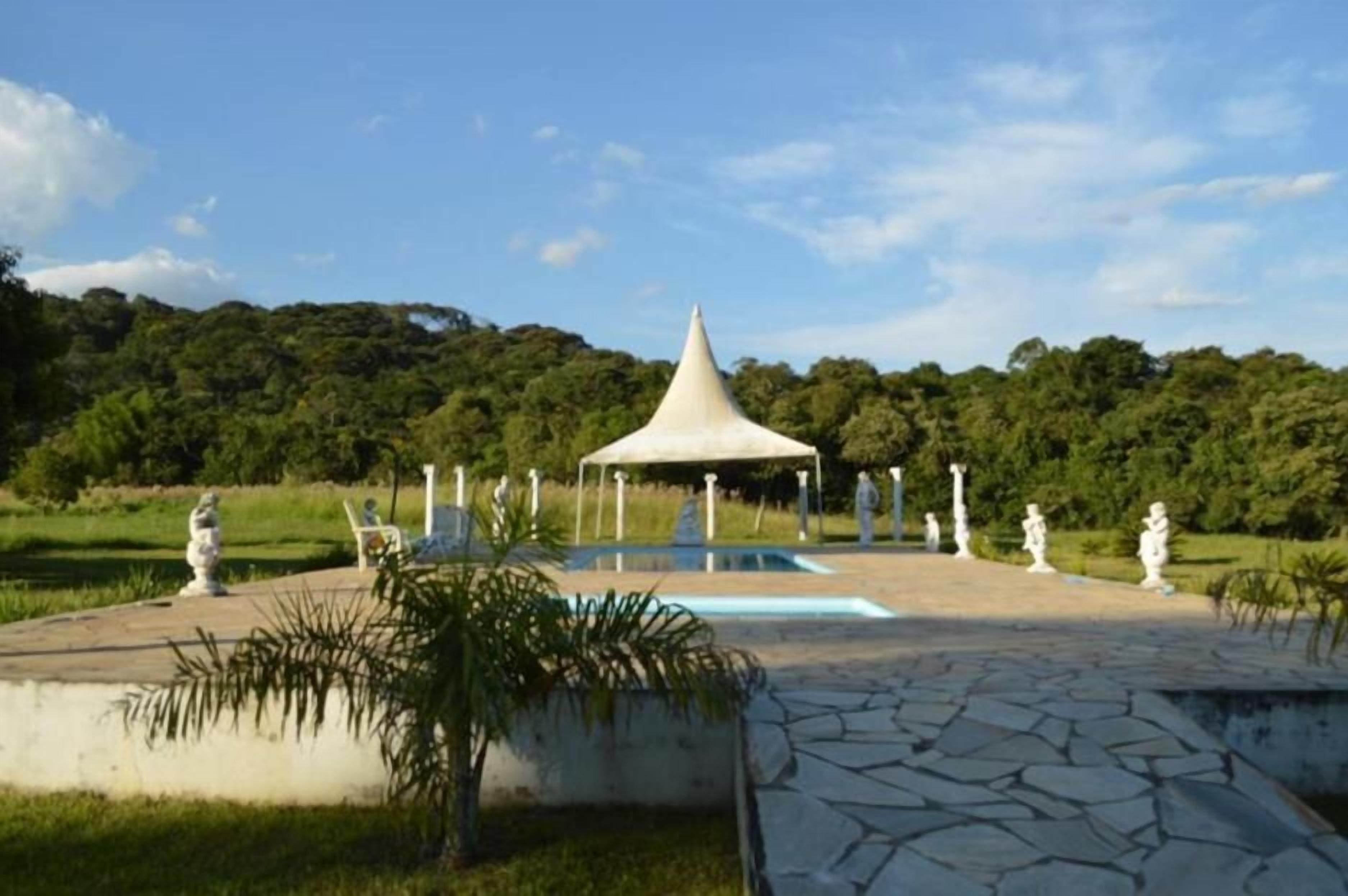 Um gazebo com telhado cônico, cercado por estátuas e uma piscina.