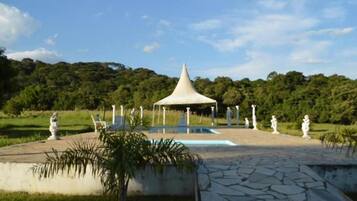 Um gazebo com telhado cônico, cercado por estátuas e uma piscina.