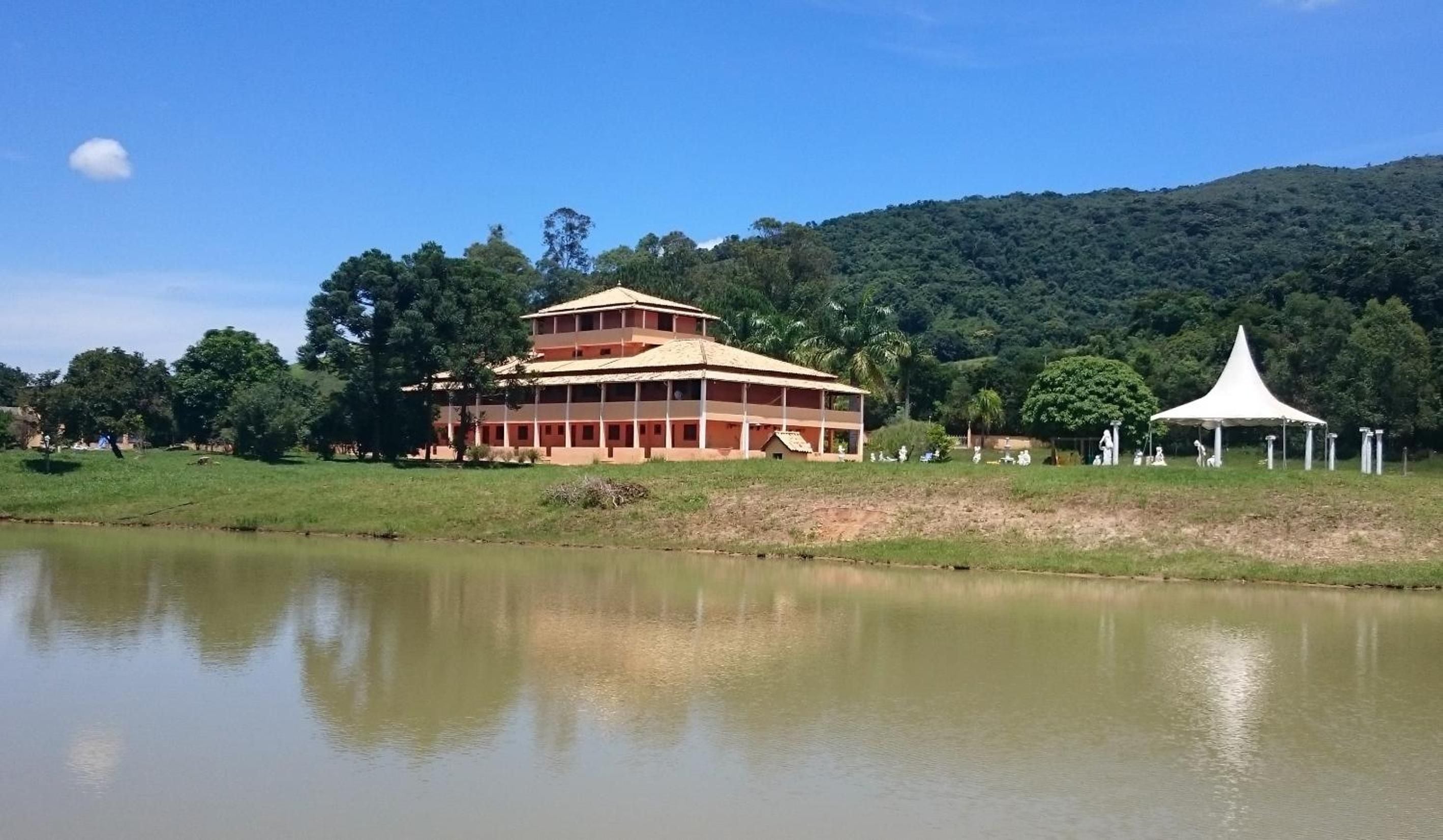 Um edifício de vários andares com telhado plano, situado perto de um corpo d'água e rodeado por vegetação.
