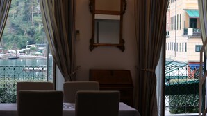 Un coin repas avec une table et des chaises, un miroir au mur et une vue sur un plan d’eau et des bâtiments, visible à travers des rideaux.