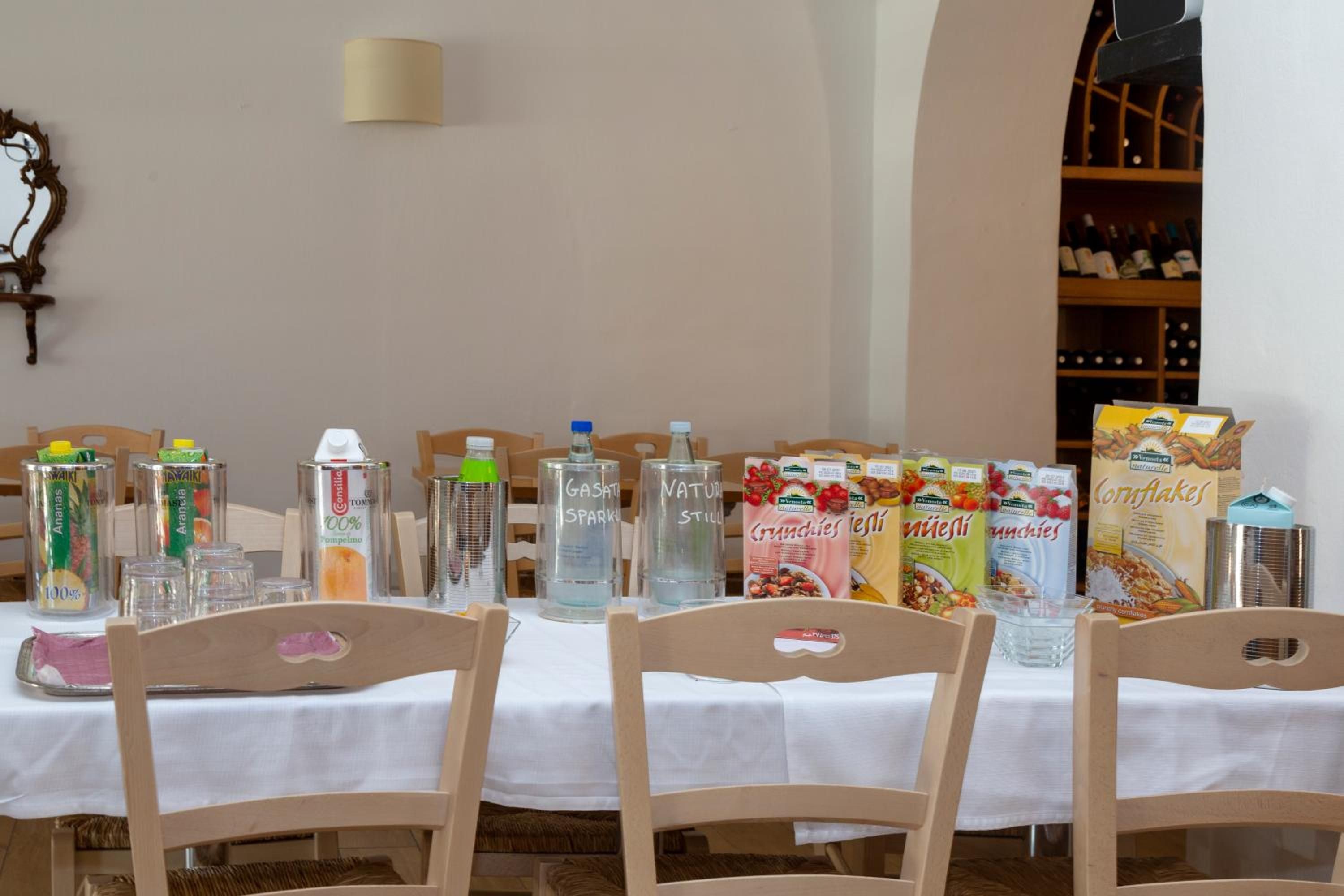 Una mesa de comedor con sillas, diversos recipientes de comida y bebida, y una estantería para vinos al fondo.