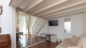 Un salon spacieux doté d’un plancher en bois, d’un canapé beige, d’un escalier et d’un téléviseur à écran plat fixé au mur.