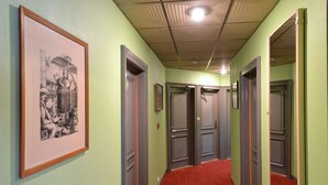 Un pasillo con paredes verdes, alfombra roja y cuadros en la pared izquierda.