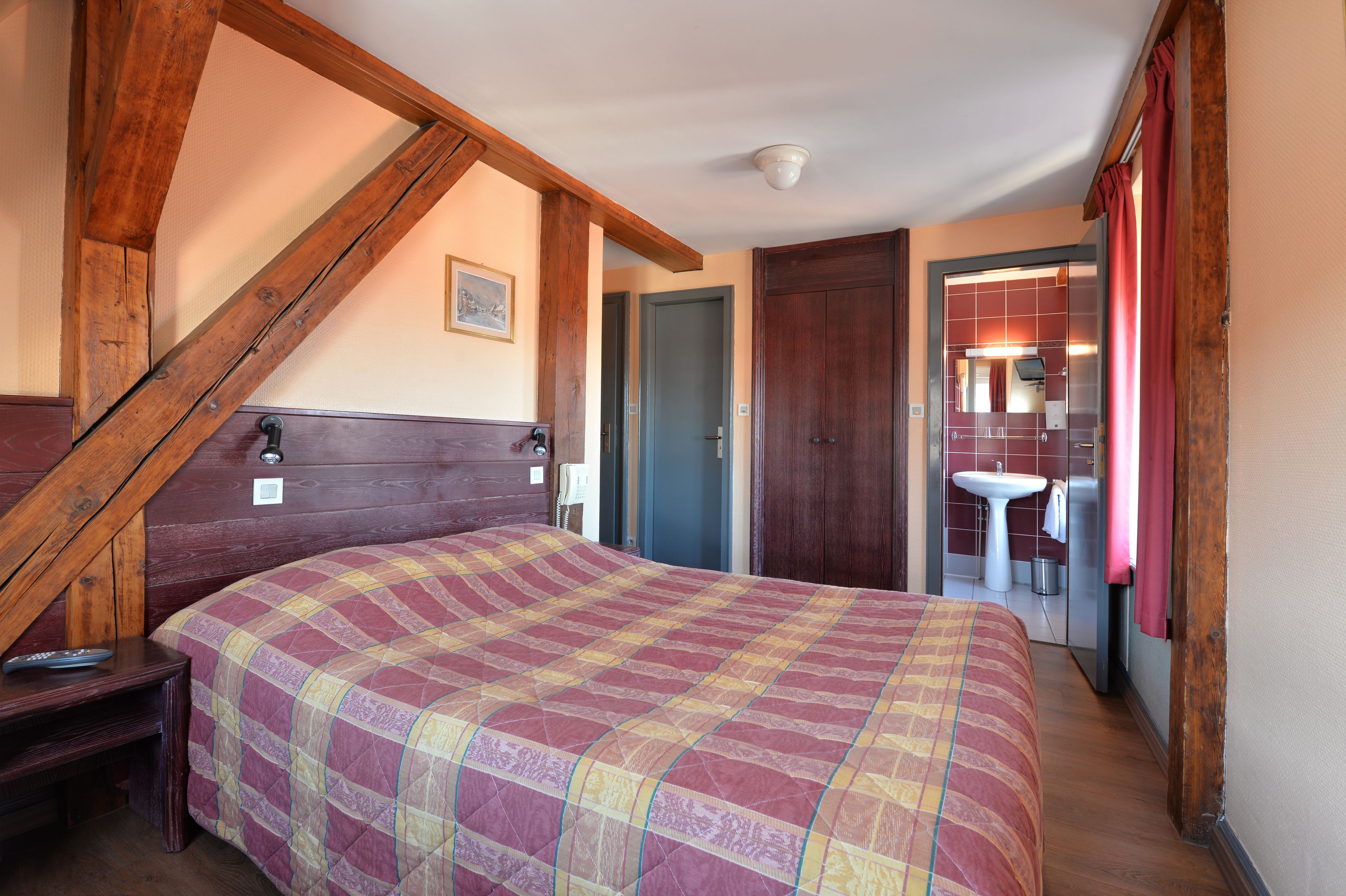 Ein Schlafzimmer mit Holzbalkendecke, einem Bett mit Quilzdecke, einem Nachttisch und einem Beistelltisch.